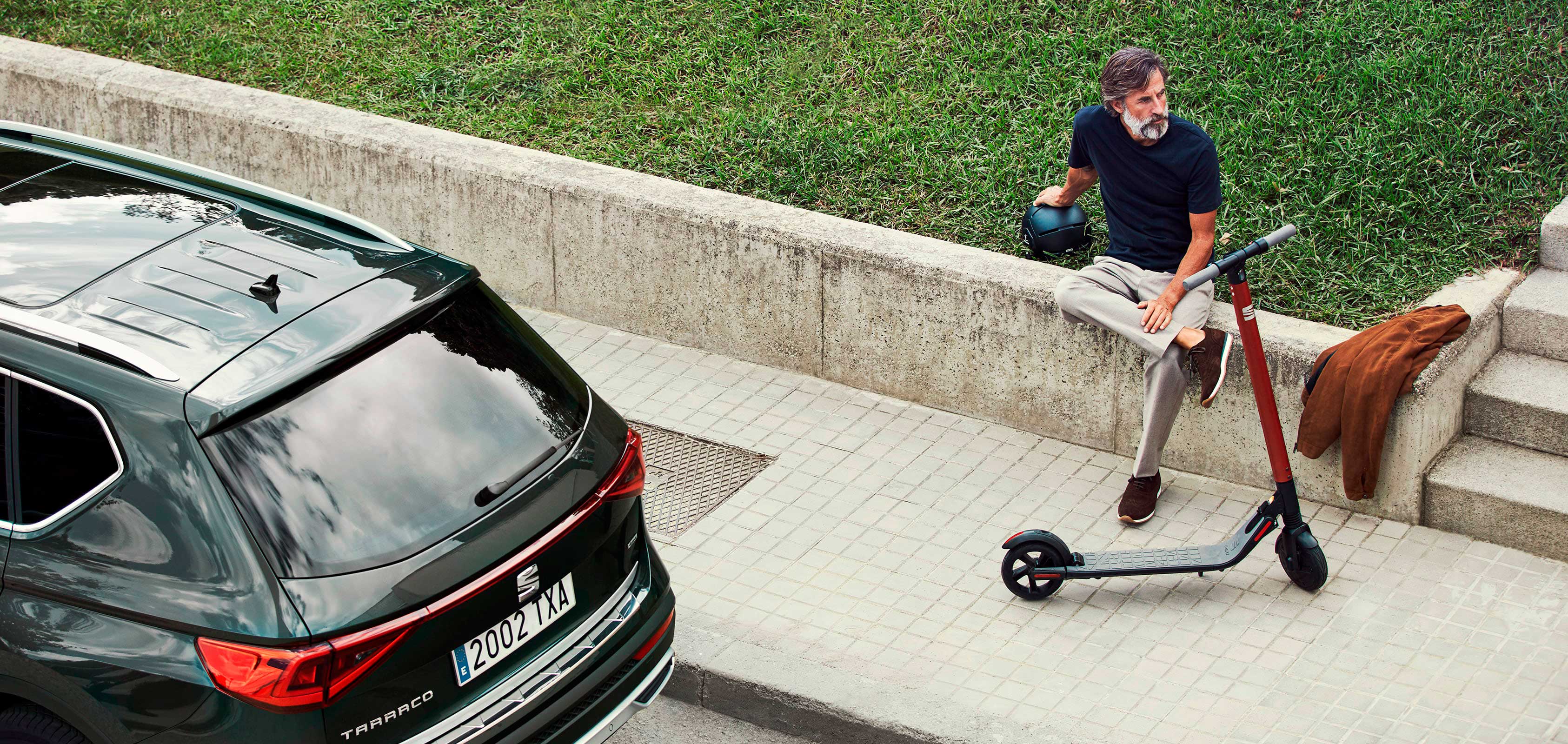 SEAT eXS KickScooter urban mobility solution powered by Segway - Man walking next to Tarraco large SUV