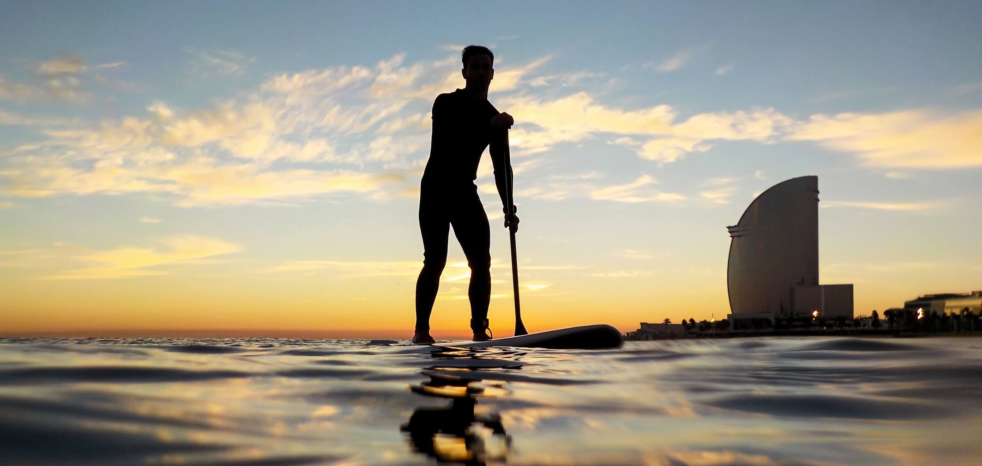 silhouette of a man paddle surfing in Barceloneta beach with the W hotel in the background